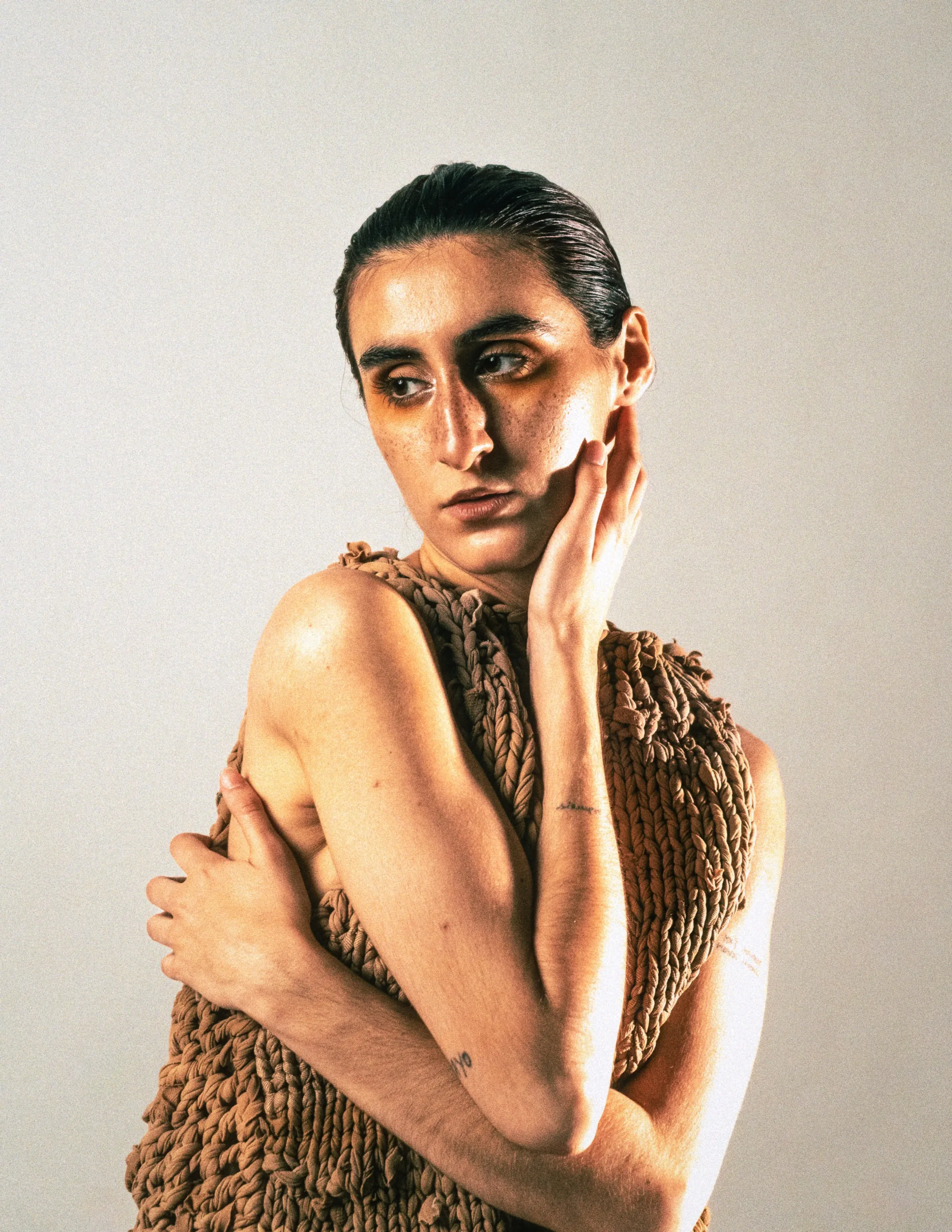 Retrato de la modelo con un top de punto artesanal y la mano sobre el rostro, sobre fondo claro.
