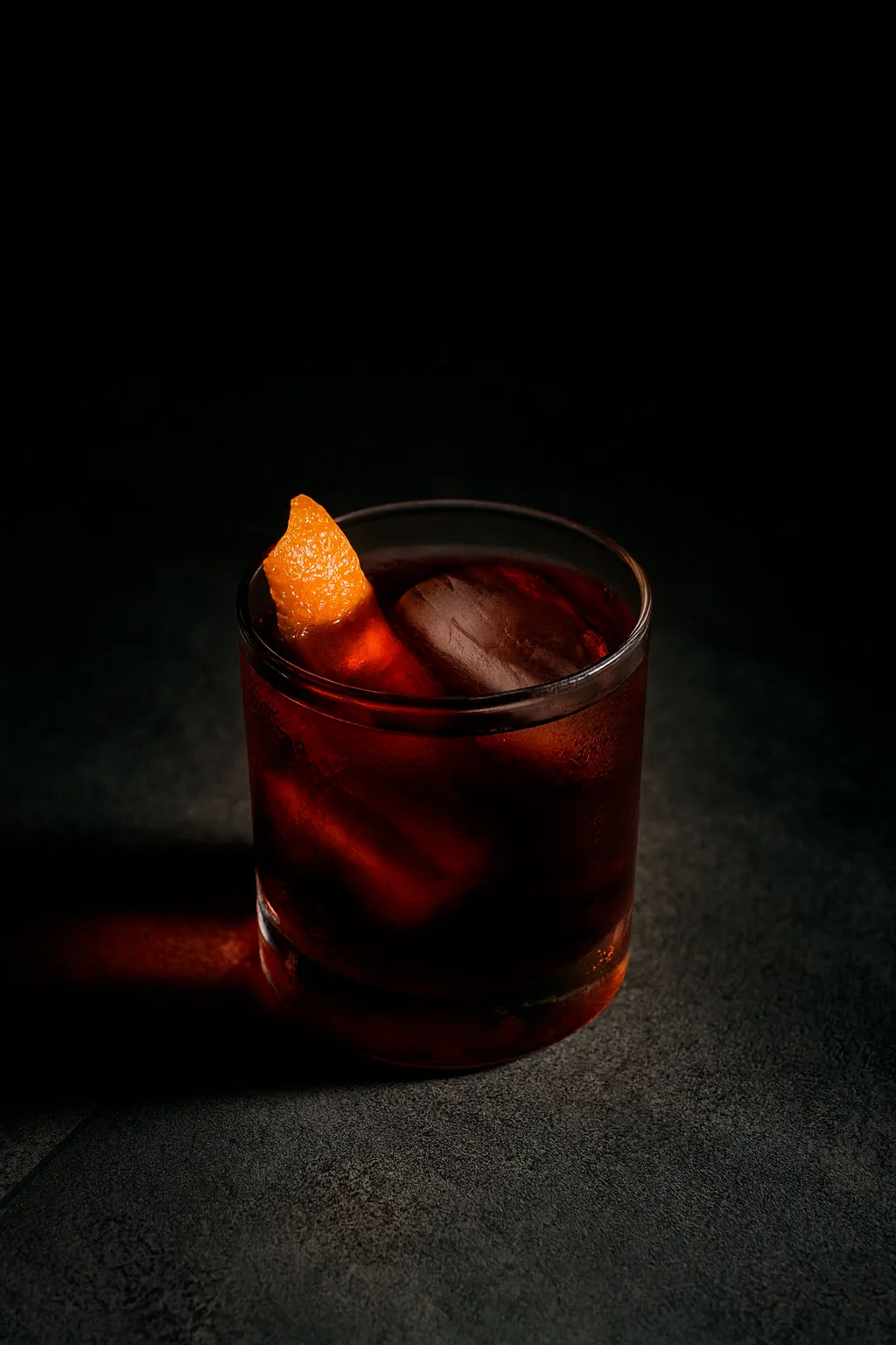 Cóctel de tono rojizo con hielo y piel de naranja en vaso bajo, uno de los más pedidos en Level 99, iluminado sobre fondo oscuro.